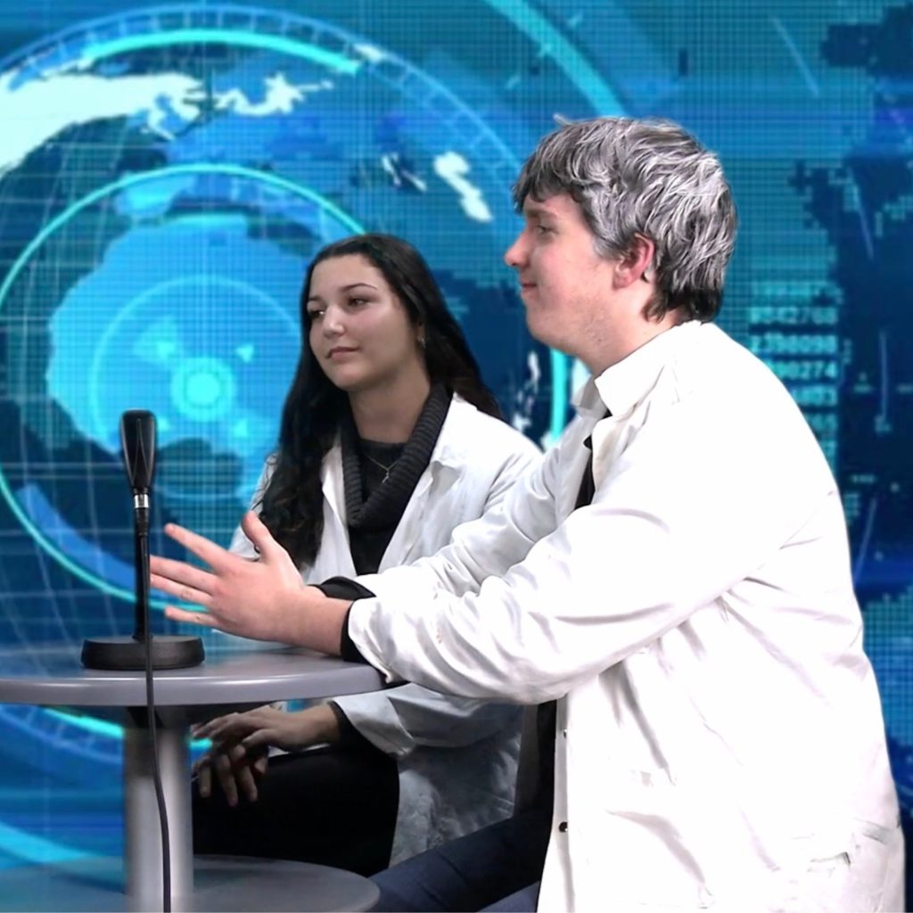 Photo d'un court métrage d'un génie de l'écologie, on peut voir le génie et sa secrétaire assis lors d'une interview avec un fond bleu.
