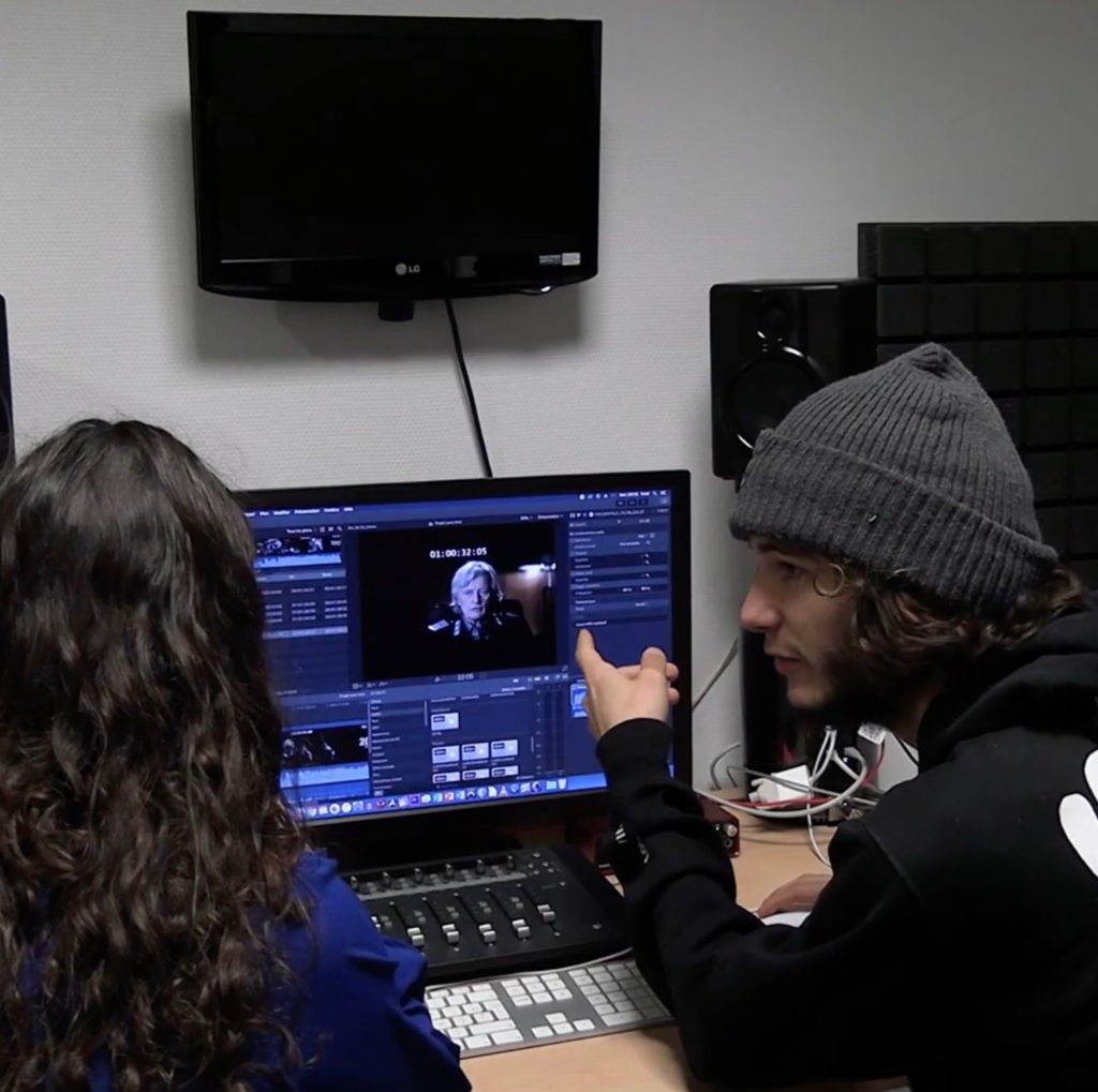 Photo du mini film de promotion du BUT MMI, on y voit deux personnes qui font du montage sur un ordinateur fixe dans une petite salle.